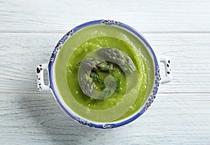 Delicious asparagus soup in bowl on white table, top view