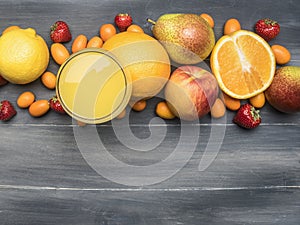 Delicious assortment of fresh variety of fruits lined around a glass with juice, kumquat, strawberry, oranges, pear, lemon, a w