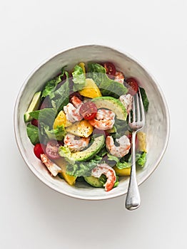 Delicious avocado, mango, shrimp, tomato salad on a ligth background, top view