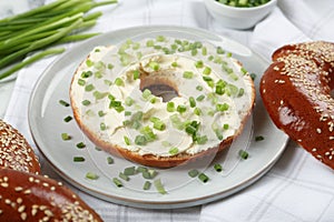 Delicious bagel with cream cheese and green onion on plate, closeup
