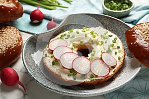 Delicious bagel with cream cheese, green onion and radish on plate, closeup