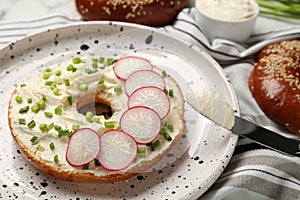 Delicious bagel with cream cheese, green onion and radish on plate, closeup