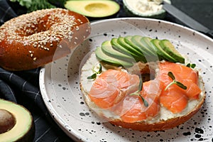 Delicious bagel with cream cheese, salmon and avocado on plate, closeup