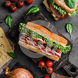Delicious baguette sandwich with ham, bacon, cheese, lettuce, tomatoes, sausage, gammon on cutting board