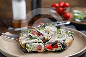 Delicious baked eggplant rolls with cheese, tomato and microgreens on plate, closeup