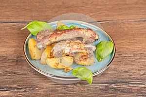 Delicious baked ribs with potatoes on a plate with basil leaves.