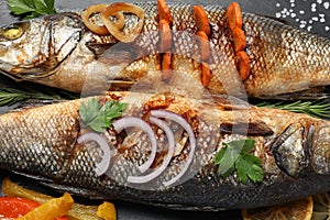 Delicious baked sea bass fish and ingredients on black plate, closeup