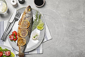 Delicious baked sea bass fish served with lemon, rosemary and sauce on light grey table, flat lay. Space for text