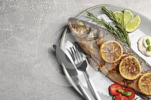 Delicious baked sea bass fish served with lemon, rosemary and sauce on light grey table, top view. Space for text