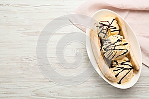 Delicious banana split ice cream with chocolate topping on white wooden table, top view. Space for text