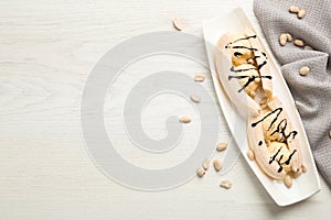 Delicious banana split ice cream portions with chocolate topping and peanuts on white wooden table, flat lay. Space for text