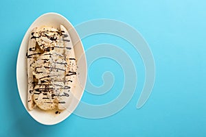 Delicious banana split ice cream with toppings on light blue background, top view. Space for text