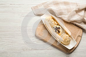 Delicious banana split ice cream with toppings on white wooden table, top view. Space for text