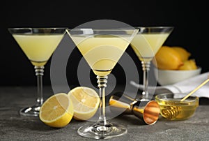 Delicious bee`s knees cocktails and ingredients on grey table against black background