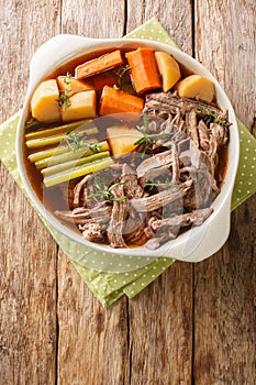 Delicious beef pot roast with potatoes, celery and carrots with thyme and rosemary closeup in the bowl. Vertical top view photo