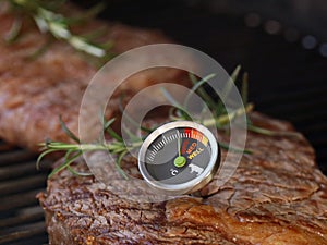 delicious beef steak on grill grate with a meat thermometer showing doneness of rare, medium and well done