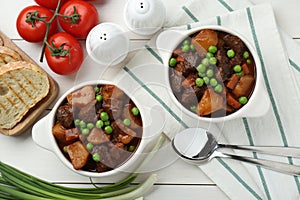 Delicious beef stew with carrots, peas and potatoes served on white wooden table, flat lay