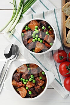 Delicious beef stew with carrots, peas and potatoes served on white wooden table, flat lay