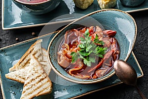 Delicious beetroot soup in bowl, solyanka with meats served with croutons over a dark background, close up view. Concept of