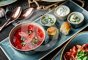 Delicious beetroot soup in bowl, traditional Russian soup with meat and cabbage served with cream and bread over dark background,