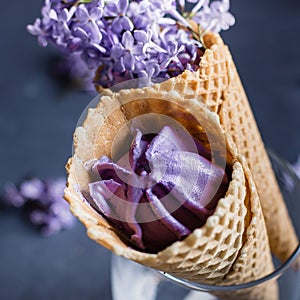 Delicious berry blackberry ice cream in waffle cone, lilac flowers. Color of the year 2022 very peri