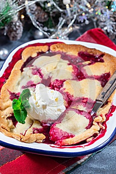 Delicious berry cobbler in enamel baking dish, garnished with ice cream, vertical