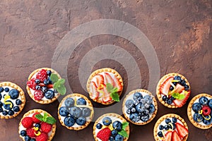 Delicious berry tartlets or cake with cream cheese decorated lemon peel and mint leaf from above. Tasty pastry desserts.