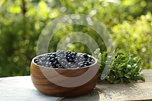 Delicious bilberries in bowl on wooden table outdoors