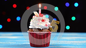 Delicious birthday cupcake with burning candle and number 5 on multicolored blurred lights background