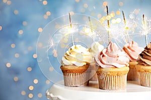 Delicious birthday cupcakes with sparklers on stand against blurred background photo