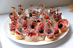 Delicious bite-size canapes of chorizo, salami on skewers served on a plate with olives