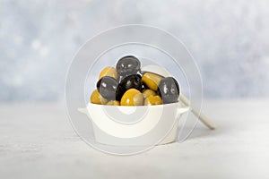 Delicious black, green and red olives with leaves in a wooden bowl on white background