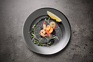 Delicious black risotto with shrimps and lemon on table, top view. Food photography