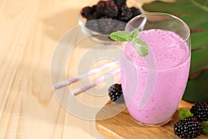 Delicious blackberry smoothie in glass and berries on wooden table, space for text