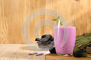 Delicious blackberry smoothie in glass and berries on wooden table, space for text