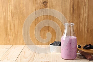 Delicious blackberry smoothie in glass bottle and fresh berries on wooden table. Space for text