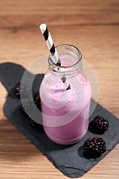 Delicious blackberry smoothie in glass bottle with straw and fresh berries on wooden table