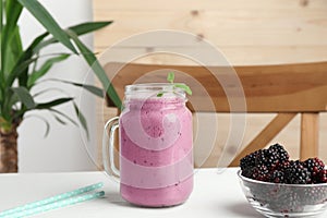 Delicious blackberry smoothie in mason jar and berries on white table indoors
