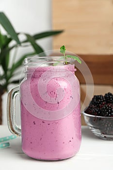 Delicious blackberry smoothie in mason jar and berries on white table indoors