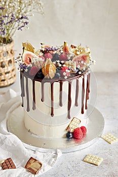 Delicious Boho Drip Cake with fruits and flowers on top on a white table