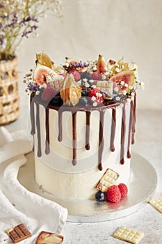 Delicious Boho Drip Cake with fruits and flowers on top on a white table