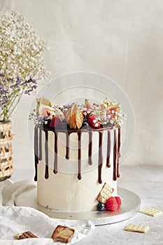 Delicious Boho Drip Cake with fruits and flowers on top on a white table