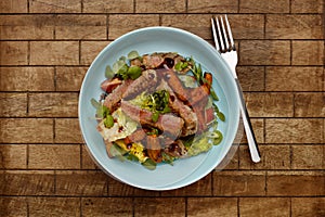 A delicious bowl of BBQ rump steak strips, sweet potatoe chips and vegetables, in a light blue bowl shot on a wooden background