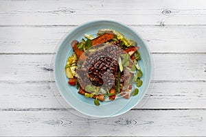 A delicious bowl of BBQ rump steak, sweet potatoe chips and vegetables, in a blue bowl on a rustic white wooden background