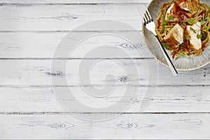 A delicious bowl of chicken chow mein, noodles and vegetables, with a fork in a rustic bowl shot on a distressed wooden background