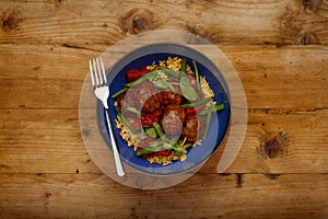 A delicious bowl of chipolte meat balls, couscous and vegetables, in a blue bowl on a rustic wooden background with a fork