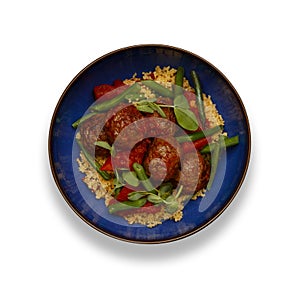 A delicious bowl of chipolte meat balls, couscous and vegetables, in a rustic blue bowl isolated on white