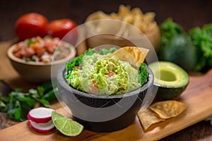 A delicious Bowl of Guacamole next to fresh ingredients on a table with tortilla chips and salsa photo