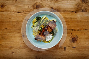 A delicious bowl of  tandoori chicken, vegetables and rice, in a blue bowl shot on a rustic wooden background