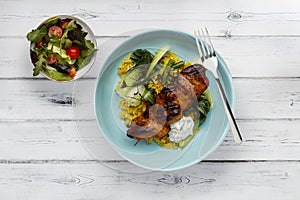 A delicious bowl of  tandoori chicken, vegetables and rice, in a light bowl shot on a rustic white wooden background with a  side